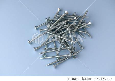 Scattered silver screws create a shiny landscape on a soft blue surface inviting creativity and craftsmanship Scattered silver screws create a shiny landscape on a soft blue surface inviting creativity and craftsmanship 142167808