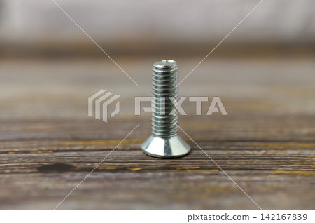 Close-up view of a shiny metal screw standing tall on a rustic wooden surface showcasing its intricate thread design and gleaming finish Close-up view of a shiny metal screw standing tall on a rustic wooden surface showcasing its intricate thread design and gleaming finish 142167839