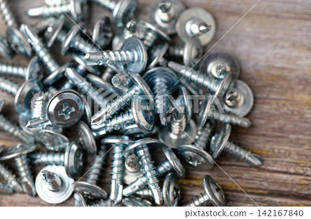 Scattered metal screws shining under soft light on a wooden surface evoke a sense of craftsmanship and the promise of new projects Scattered metal screws shining under soft light on a wooden surface evoke a sense of craftsmanship and the promise of new projects 142167840