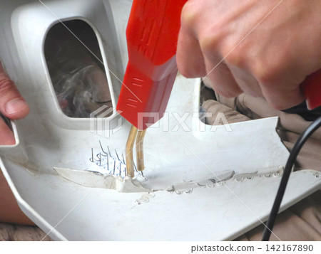 Man repairing plastic bumper with hot stapler tool. Automotive technician fixing crack on car body part. Professional vehicle bodywork and restoration service, maintenance concept. Man repairing plastic bumper with hot stapler tool. Automotive technician fixing crack on car body part. Professional vehicle bodywork and restoration service, maintenance concept. 142167890