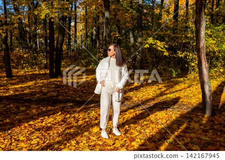 Woman hiking through an autumn forest covered with fallen leaves. Seasonal outdoor recreation, nature walk, peaceful travel and healthy lifestyle concept. Woman hiking through an autumn forest covered with fallen leaves. Seasonal outdoor recreation, nature walk, peaceful travel and healthy lifestyle concept. 142167945
