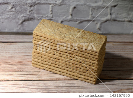 Stack of rectangular crispbread on a wooden surface against a white brick wall Stack of rectangular crispbread on a wooden surface against a white brick wall 142167990