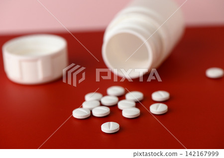 Pills scattered around an open medication bottle on a vibrant red surface evoke a sense of health and wellness during a quiet moment in a cozy home Pills scattered around an open medication bottle on a vibrant red surface evoke a sense of health and wellness during a quiet moment in a cozy home 142167999