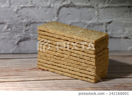Stack of rectangular crispbread on a wooden surface against a white brick wall Stack of rectangular crispbread on a wooden surface against a white brick wall 142168001