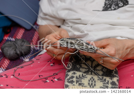 Person holding a patterned wool sock in progress with double-pointed needles Person holding a patterned wool sock in progress with double-pointed needles 142168014