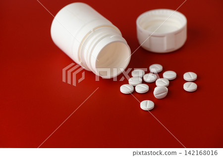 White tablets scattered near an overturned medicine bottle on a vibrant red surface 142168016