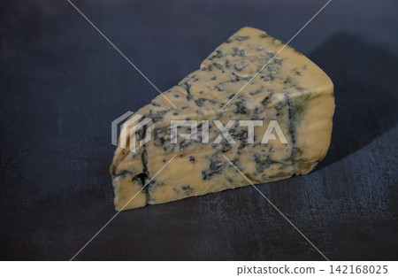 Delicious blue cheese piece resting on a dark surface, showcasing its rich texture and unique veining Delicious blue cheese piece resting on a dark surface, showcasing its rich texture and unique veining 142168025