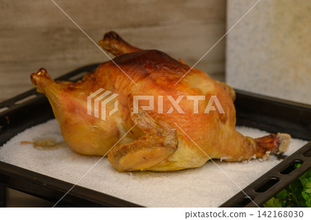 Juicy roast chicken resting on a bed of salt, ready to be served in a cozy kitchen at twilight Juicy roast chicken resting on a bed of salt, ready to be served in a cozy kitchen at twilight 142168030