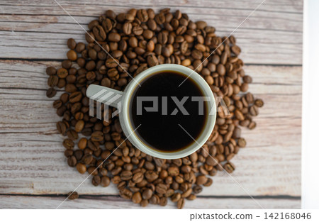 Top down flatlay of white coffee cup and roasted beans on light wood Top down flatlay of white coffee cup and roasted beans on light wood 142168046