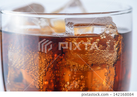 Crystal clear ice cubes floating in refreshing cola beverage with carbonation bubbles Crystal clear ice cubes floating in refreshing cola beverage with carbonation bubbles 142168084