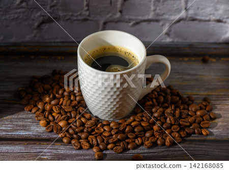 Coffee cup nestled in a sea of roasted beans, inviting warmth and aroma on a rustic wooden table 142168085