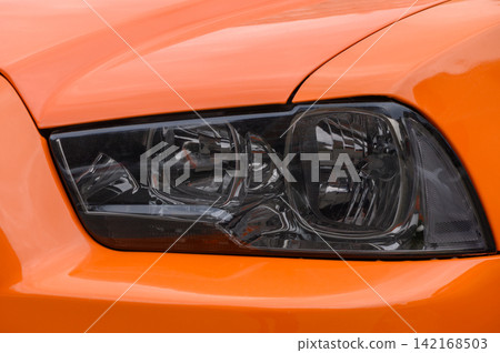 Macro close-up of the tinted headlight and orange hood panel of a Dodge Charger Macro close-up of the tinted headlight and orange hood panel of a Dodge Charger 142168503