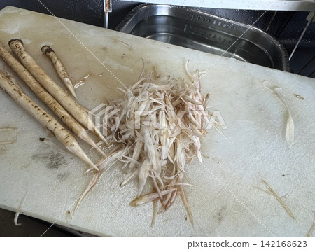 砧板上堆放著一堆切絲的牛蒡根和牛蒡根。 砧板上堆放著一堆切絲的牛蒡根和牛蒡根。 142168623