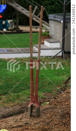 Post Hole Digger Tool Stands in a Yard With Green Grass Around Post Hole Digger Tool Stands in a Yard With Green Grass Around 142168912