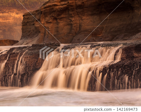 Long exposure photography of silky smooth water cascading over rocky cliff terraces at Klayar Beach (Pantai Klayar) during warm golden hour sunrise, Pacitan, East Java, Indonesia. Long exposure photography of silky smooth water cascading over rocky cliff terraces at Klayar Beach (Pantai Klayar) during warm golden hour sunrise, Pacitan, East Java, Indonesia. 142169473