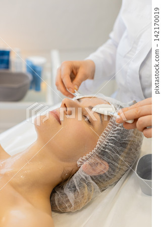Cosmetologist applies cleansing foam with soft brushes on Caucasian woman face in beauty clinic spa Cosmetologist applies cleansing foam with soft brushes on Caucasian woman face in beauty clinic spa 142170019
