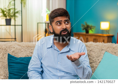 Indian man rolls eyes ironic reaction shows disbelief sarcasm during smartphone conversation indoors Indian man rolls eyes ironic reaction shows disbelief sarcasm during smartphone conversation indoors 142170027