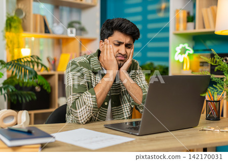 Indian man on home table looks tired at laptop with burnout after hard remote work session indoors Indian man on home table looks tired at laptop with burnout after hard remote work session indoors 142170031