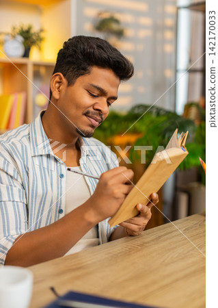 Indian man on home table reading book making notes and thinking deeply during focused study at home Indian man on home table reading book making notes and thinking deeply during focused study at home 142170033