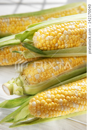 Fresh corn cobs with green husks on white wooden table Fresh corn cobs with green husks on white wooden table 142170040