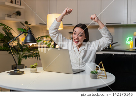 Young woman sees approved grant on laptop celebrates raises hand smiles excited big reaction evening Young woman sees approved grant on laptop celebrates raises hand smiles excited big reaction evening 142170146