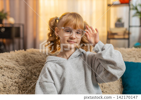 Young teenager girl putting on glasses with a focused expression indoors at home sitting on sofa Young teenager girl putting on glasses with a focused expression indoors at home sitting on sofa 142170147