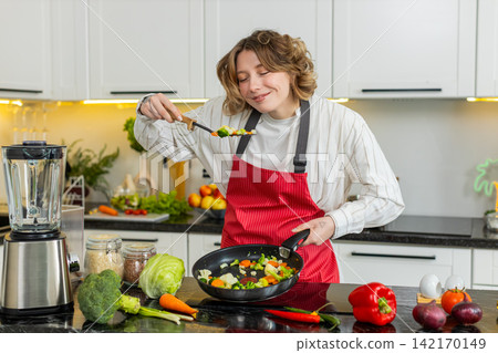 Young woman tasting cooked vegetables in kitchen while making healthy dinner for clean eating habit Young woman tasting cooked vegetables in kitchen while making healthy dinner for clean eating habit 142170149