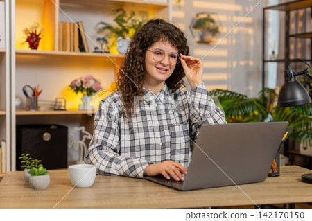 Young woman on home table putting on glasses for reading and office work with confident focused look Young woman on home table putting on glasses for reading and office work with confident focused look 142170150