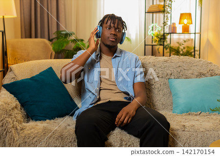 African American young man on home sofa listens to podcast in headphones while nodding in agreement African American young man on home sofa listens to podcast in headphones while nodding in agreement 142170154
