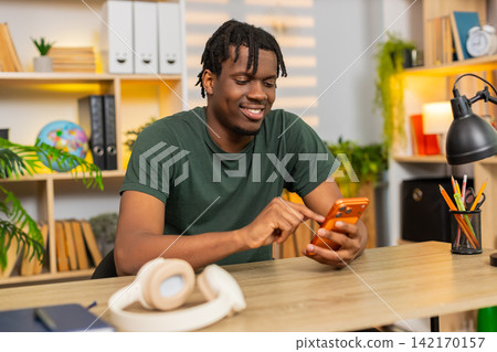 African American young man on home table using smartphone reading message with happy smile indoors 142170157