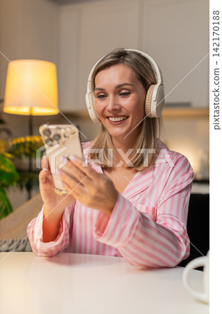 Adult woman in headphones laughs at podcast on smartphone posts like review in app enjoys content Adult woman in headphones laughs at podcast on smartphone posts like review in app enjoys content 142170188