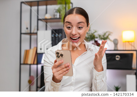 Young businesswoman typing fast on smartphone reads news of app game win and raises fist in victory Young businesswoman typing fast on smartphone reads news of app game win and raises fist in victory 142170334