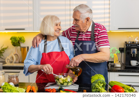 Senior old woman man smiling pouring dressing on fresh salad in home kitchen for diet wellness plan Senior old woman man smiling pouring dressing on fresh salad in home kitchen for diet wellness plan 142170340