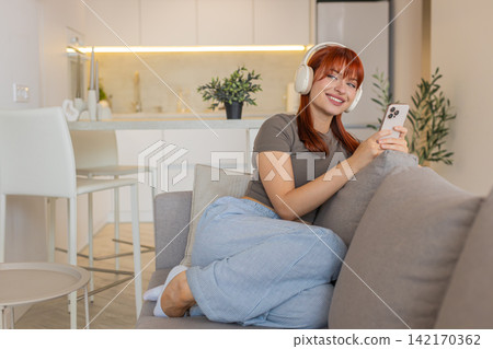 Young woman in wireless headphones listens to music on smartphone relax chill calm mood and breathe Young woman in wireless headphones listens to music on smartphone relax chill calm mood and breathe 142170362