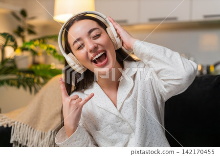 Young woman hears song in headphones starts seated dance rock moves laughs cheers yeah energy wild Young woman hears song in headphones starts seated dance rock moves laughs cheers yeah energy wild 142170455
