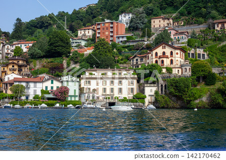 Multicolor houses building architecture on lake Como, Italy city on mountain. Boats on water waves 142170462