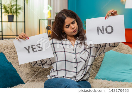 Indian woman hesitates holding yes and no signs displaying decision doubt confusion needing answer Indian woman hesitates holding yes and no signs displaying decision doubt confusion needing answer 142170463