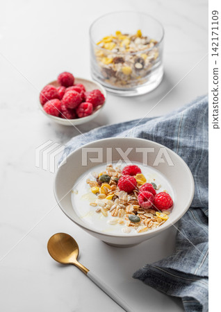 Natural Greek yogurt with muesli, raspberries and honey in a bowl on a marble background Natural Greek yogurt with muesli, raspberries and honey in a bowl on a marble background 142171109