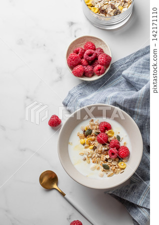 Diet low-fat yogurt with muesli, raspberries and honey in a bowl on a marble background Diet low-fat yogurt with muesli, raspberries and honey in a bowl on a marble background 142171110