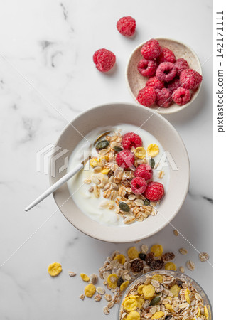 Diet low-fat yogurt with muesli, raspberries and honey in a bowl on a marble background Diet low-fat yogurt with muesli, raspberries and honey in a bowl on a marble background 142171111