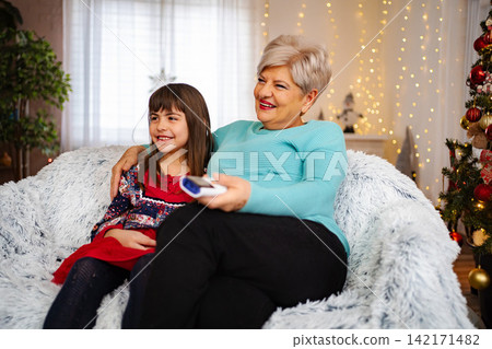 Grandmother and granddaughter smiling, relaxing on sofa during Christmas Grandmother and granddaughter smiling, relaxing on sofa during Christmas 142171482