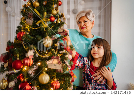 Grandmother and granddaughter decorating Christmas tree together at home Grandmother and granddaughter decorating Christmas tree together at home 142171486