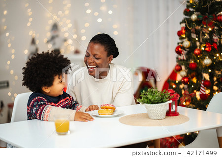 Mother and son enjoying Christmas breakfast with donuts Mother and son enjoying Christmas breakfast with donuts 142171499