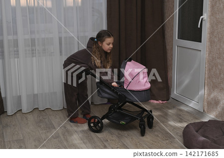 Little girl pushes toy baby stroller across room. Little girl pushes toy baby stroller across room. 142171685