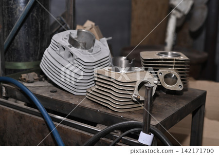 Disassembled motorcycle cylinder blocks lie on workshop table during repair. Disassembled motorcycle cylinder blocks lie on workshop table during repair. 142171700