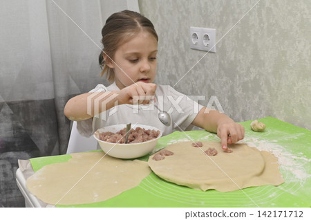 girl making dumplings with minced meat at kitchen table, girl placing filling on rolled dough, home cooking process, child learning kitchen skill, traditional meal preparation, cozy interior girl making dumplings with minced meat at kitchen table, girl placing filling on rolled dough, home cooking process, child learning kitchen skill, traditional meal preparation, cozy interior 142171712