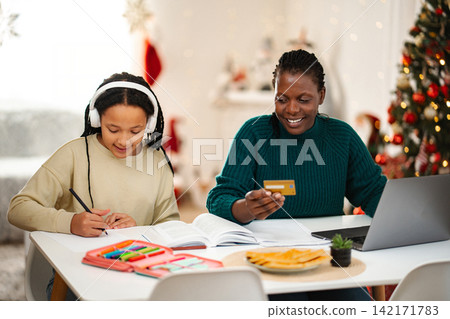 Mother and daughter celebrating Christmas, shopping online and studying Mother and daughter celebrating Christmas, shopping online and studying 142171783