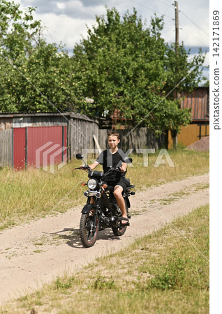 Young boy rides small moped along dirt country road. Young boy rides small moped along dirt country road. 142171869