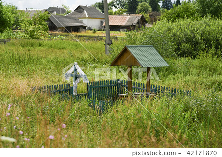 Wooden well stands near roadside cross in green rural meadow. Wooden well stands near roadside cross in green rural meadow. 142171870