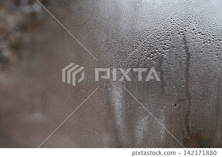wet glass abstract background. Steam on window with blurred water droplets, showing trees outside in the distance. perfect for cold or rainy weather moods. drops on pane of window wet glass abstract background. Steam on window with blurred water droplets, showing trees outside in the distance. perfect for cold or rainy weather moods. drops on pane of window 142171880
